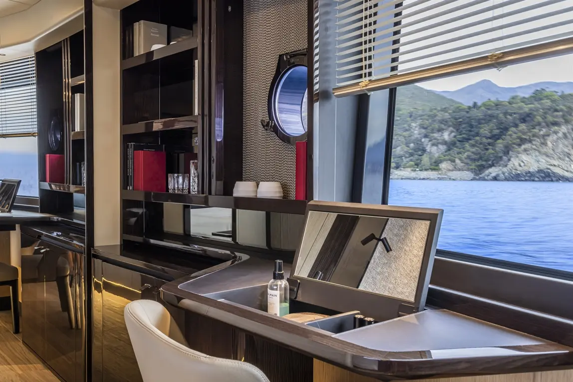 Luxury yacht interior featuring sleek furniture, a desk with a mirror, and scenic sea views through a round window.